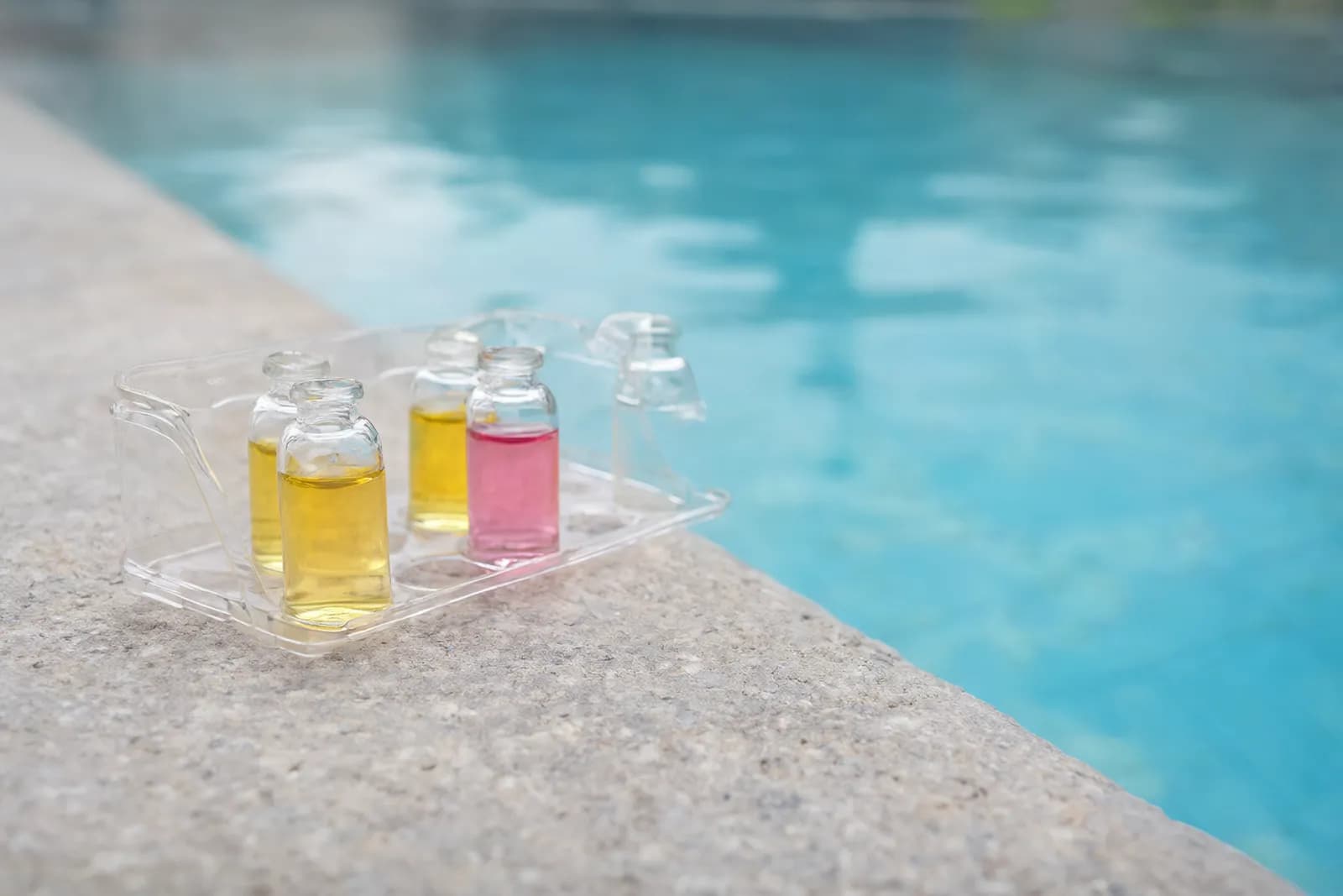 A pool test kit with reagent bottles and a comparator block on a sunlit ledge